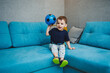 © Дмитрий Ткачук - A two-year-old little boy sits on the sofa with a ball in his hands. A developed emotional boy plays with a ball at home