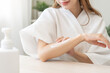 © KMPZZZ - Health care, beauty smile pretty asian young woman in bathrobe, towel after shower bath at home, hand applying, putting moisturizer on her arm. Skin body cream moisturizing lotion, routine in morning.