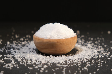 Wall Mural - salt into a wooden spoon from a bowl on a black background. Coarse sea salt.