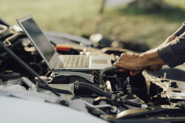 Young mechanic opens the bonnet to inspect the engine for damage and does professional maintenance. He puts on his uniform and inspects.