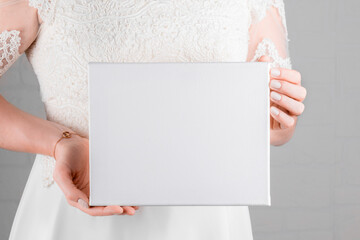Poster - Bride holding white canvas mockup on white wall background. Minimal stile blank mockup, picture mockup, template canvas mockup for art work or presentation your design