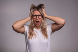 Fototapeta  - The young woman is angry and screaming, holding her head