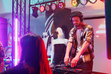Dj in headphones mixing tracks at electronic music concert in nightclub. Musician performing using digital panel on stage with spotlights at disco party for clubbers crowd