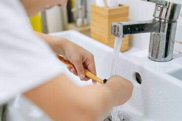 Wall Mural - child is rinsing bamboo tooth brus with water running from sink tap