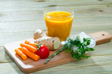 Wall Mural - Image of healthy fresh carrot juice with ginger, served at wooden desk with vegetables and greens