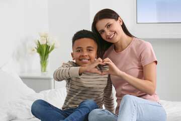 Wall Mural - Mother and her African American son making heart with hands on bed at home. International family