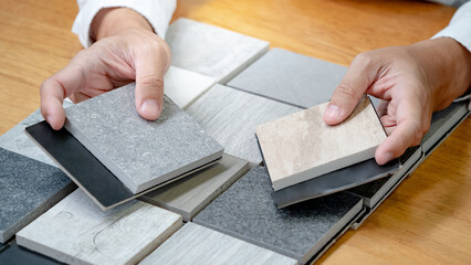 Architect hand choosing sample of stone material or tile texture collection on the table in studio. Designer working for interior architecture and furniture design project.
