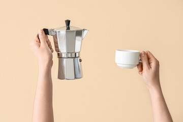 Wall Mural - Female hands holding cup and geyser coffee maker on beige background