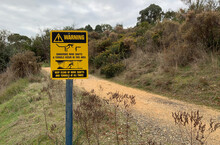 Black And Yellow Warning: Dangerous Mine Shafts And Tunnels Occur In This Area - Keep Clear At All Times Metal Sign On Post Near Walking Track