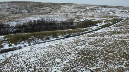 Sticker - Drone shot of a car driving on a narrow road in snowy landscape