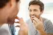© HockleyMedia/peopleimages.com - Teeth, morning routine and mirror with man in bathroom for self care, oral hygiene and dental. Cleaning, smile and health with face of male person at home for beauty, wellness and reflection