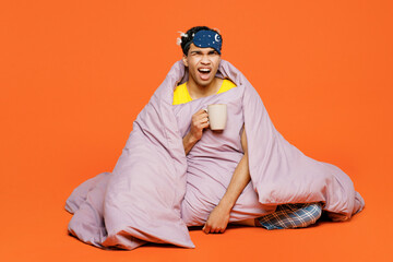 Wall Mural - Full body sad tired young man wear pyjamas jam sleep eye mask rest relax at home drink coffee holding cup look camera isolated on plain orange background studio portrait. Good mood night nap concept.