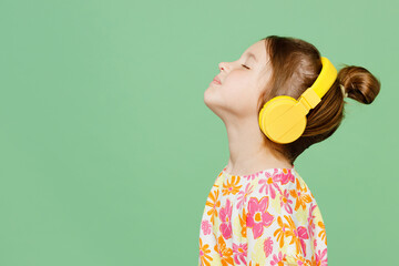 Wall Mural - Side view little child kid girl 6-7 year old in casual clothes headphones listen music close eyes isolated on plain pastel green background studio portrait Mother's Day love family lifestyle concept