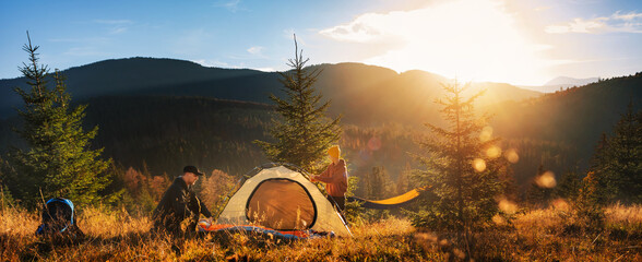 two tourists pitch tent in the mountains at sunset. family vacation in mountains.