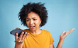 © HockleyMedia/peopleimages.com - Confused, phone and african woman isolated on blue background for college doubt, decision or questions. Voice, call and young person or student with what or why hand for mobile problem or choice