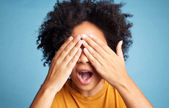 Shock, scared and woman closing her eyes in a studio for fear, horror or panic expression. Surprise, emotion and crazy female model with a cant look gesture or emoji isolated by a blue background.
