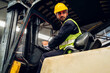 © kanpisut - Man worker at forklift driver happy working in industry factory logistic ship. Man forklift driver in warehouse area. Forklift driver sitting in vehicle in warehouse.
