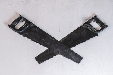 Two crossed black hand saw on a white stucco wall, closeup