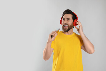 Canvas Print - Emotional man singing while listening music with headphones on light grey background. Space for text