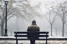 Man Sitting On Bench In Snow Park In Winter. Cold And Solitude