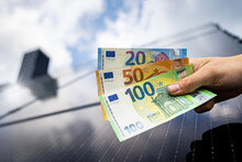 Euro Banknotes In A Hand With A Solar Panel Roof In The Background