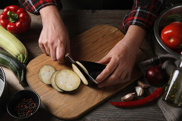 Cooking delicious ratatouille. Woman cutting fresh eggplant at wooden table, closeup