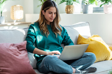 Beautiful kind woman working with laptop while sitting on couch in living room at home