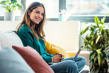 Beautiful kind woman working with laptop while sitting on couch in living room at home