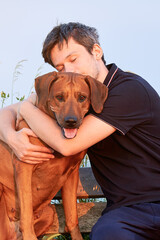 Young man snuggling and hugging his dog sitting outdoors. Close friendship, love and bond between owner and pet 