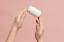 White Bottle (plastic Tube) In Hands On Pink Background. Packaging For Vitamins, Pill Or Capsule, Or Supplement. Mockup For Product Branding