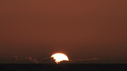 Wall Mural - Time lapse of sun rising behind low horizon clouds and into a warm clear sky over water, night to day transition.