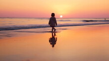 Small Baby Walk On Sunset At Beach Sand ,sunbeam Flares And Reflection On Sea Water ,generated Ai