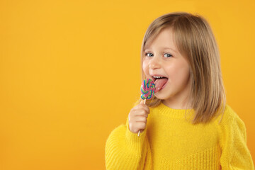 Wall Mural - Portrait of cute girl licking lollipop on orange background, space for text