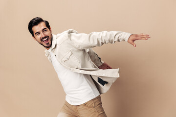 Poster - Stylish man smile runs and jumps on a beige background in a white t-shirt and business jacket, flying clothes hero, fashionable clothing style, copy space, space for text