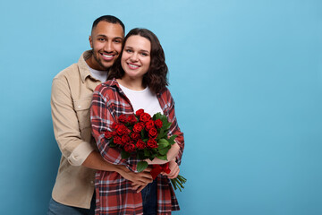 Poster - Happy couple celebrating Valentine's day. Beloved woman with bouquet of red roses on light blue background. Space for text