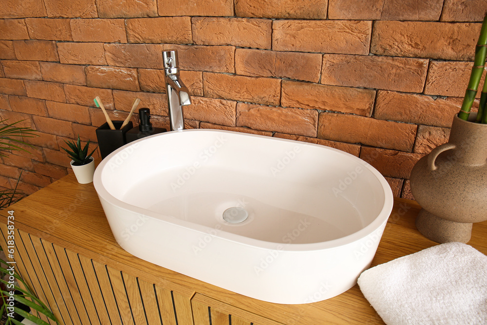 Sink with bath accessories on table near brick wall