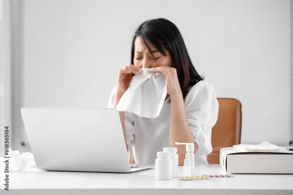 Ill Asian businesswoman with tissue in office