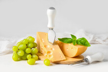 Wooden Board With Tasty Swiss Cheese And Grapes On Light Background