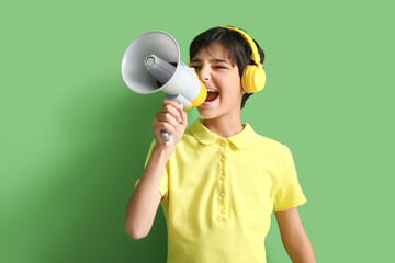 Wall Mural - Little boy with headphones shouting into megaphone on green background