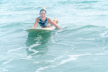 Asian women wearing strong swimsuits hobby surfing waves Lying on the board waiting for the big wave to come from the sea is an exciting water sport on the beach in Thailand.