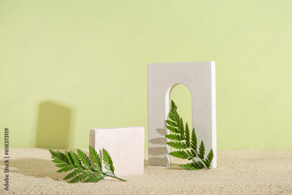 Decorative plaster podiums with fern leaves on sand against olive background