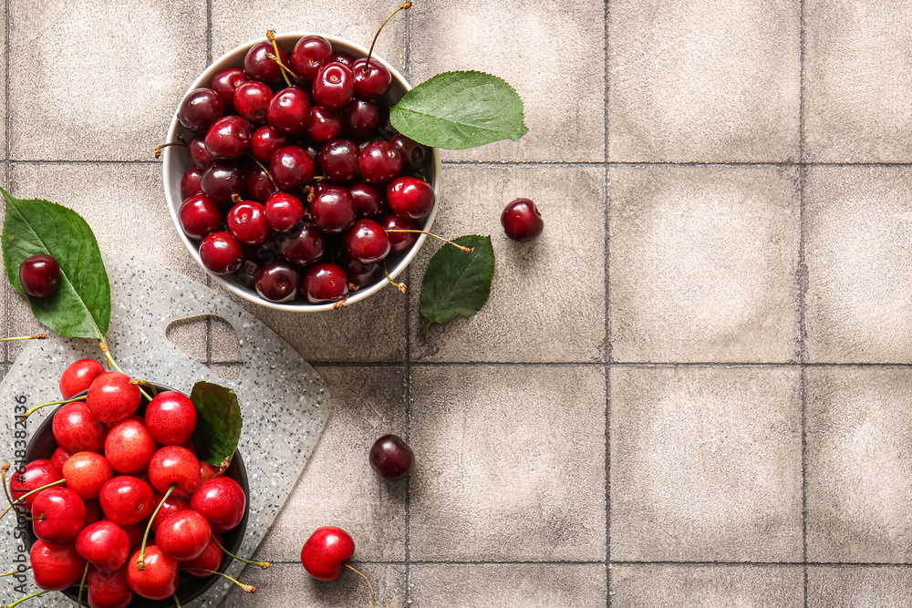 Bowls with sweet cherries on grey tile background