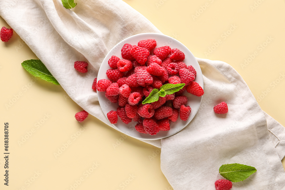 Plate with fresh raspberries and mint on yellow background