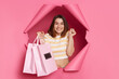 © sementsova321 - Extremely happy smiling brunette woman wearing striped t shirt posing in torn pink paper wall holding shopping bags clenched fist rejoicing her cool shopping.