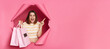 © sementsova321 - Amazed surprised caucasian young woman wearing striped shirt breaking through pink paper hole holding shopping bags pointing away at copy space for advertisement blank wall.