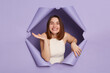 © sementsova321 - Cute smiling happy young brunette woman in casual clothing breaking through purple paper hole looking at camera with positive facial expression.