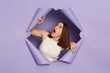 © sementsova321 - Shocked young brunette woman in casual clothing breaking through purple paper hole looking up with widely open mouth sees something amazement.