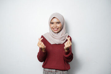 Wall Mural - Beautiful smiling Asian woman in red sweater showing Korean heart with two fingers crossed, express joy and positivity isolated over white background