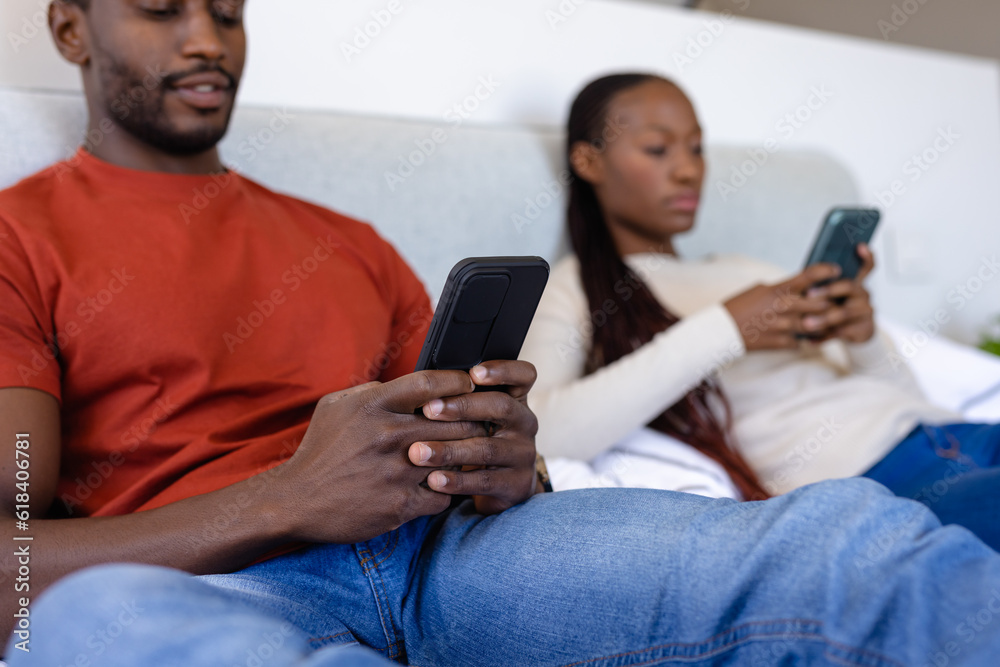 African american couple using smartphones lying on bed in bedroom Stock ...
