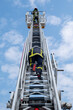 © shocky - Des pompiers sur une grande échelle et un ciel bleu avec des nuages